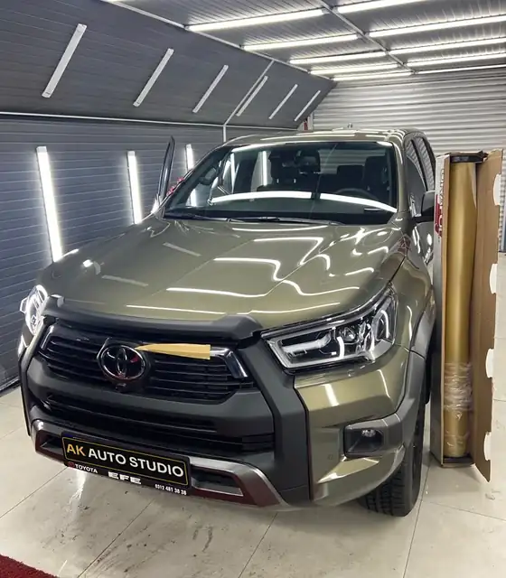 Kaplama öncesi haki renkli Toyota Hilux atölyede, yanında altın folyo rulosu