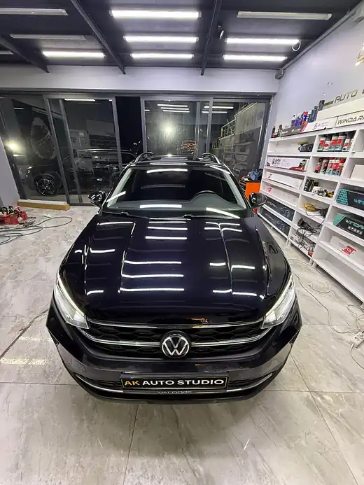 Kaputunda ışıklar yansıyan siyah Volkswagen önden, yanında ürün rafları